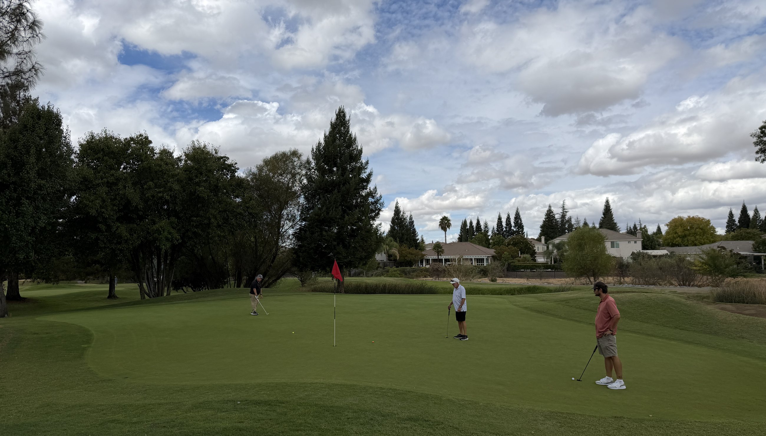 Two golfers putting out on a Diamond Oaks green under a broad Sacramento Valley sky