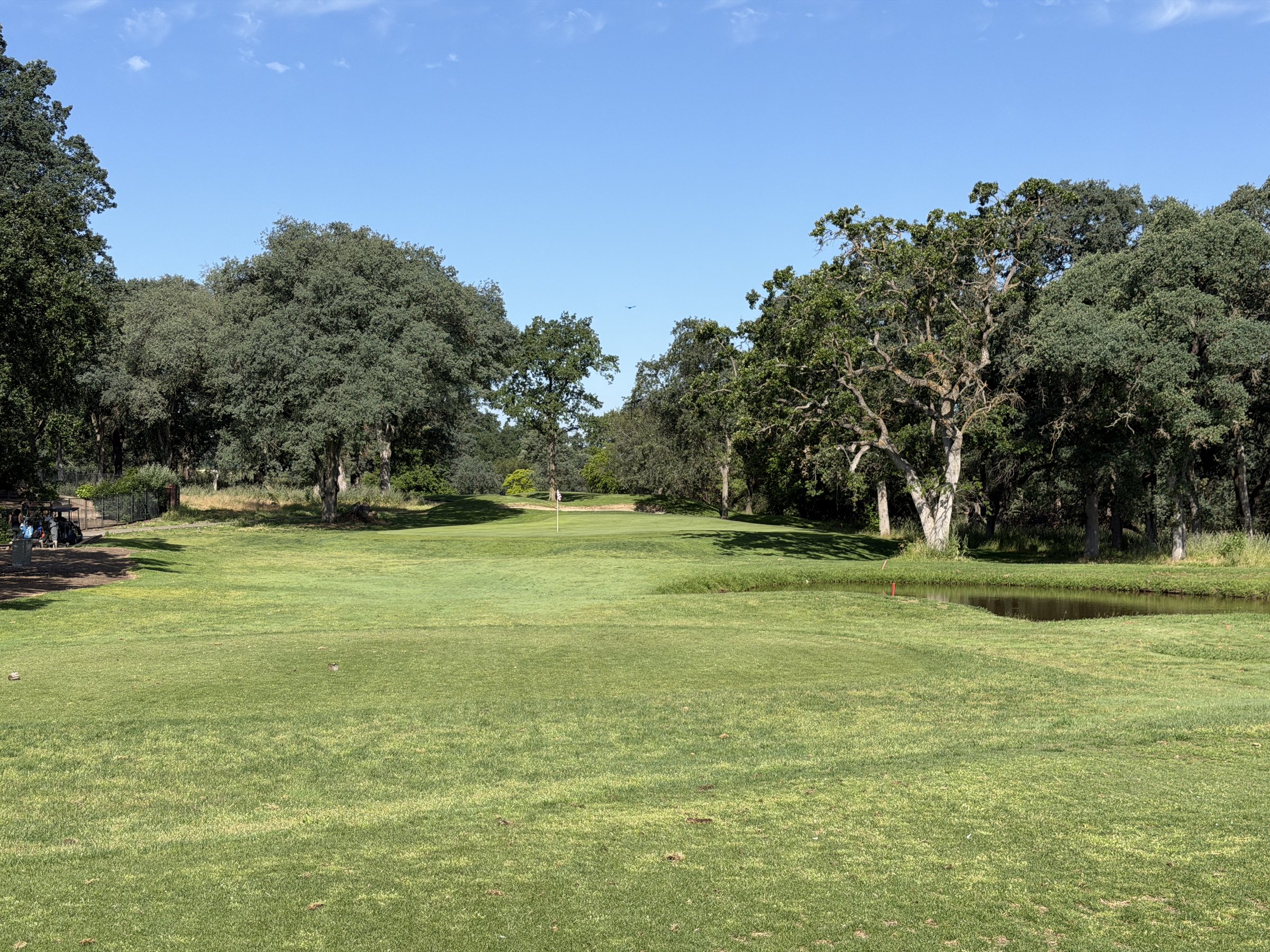 A wide fairway at Woodcreek Golf Club framed by mature valley oaks, water short of the green