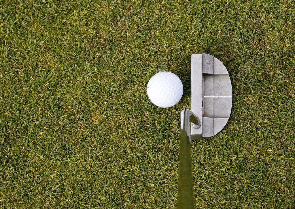A putter squared behind a ball on the practice green