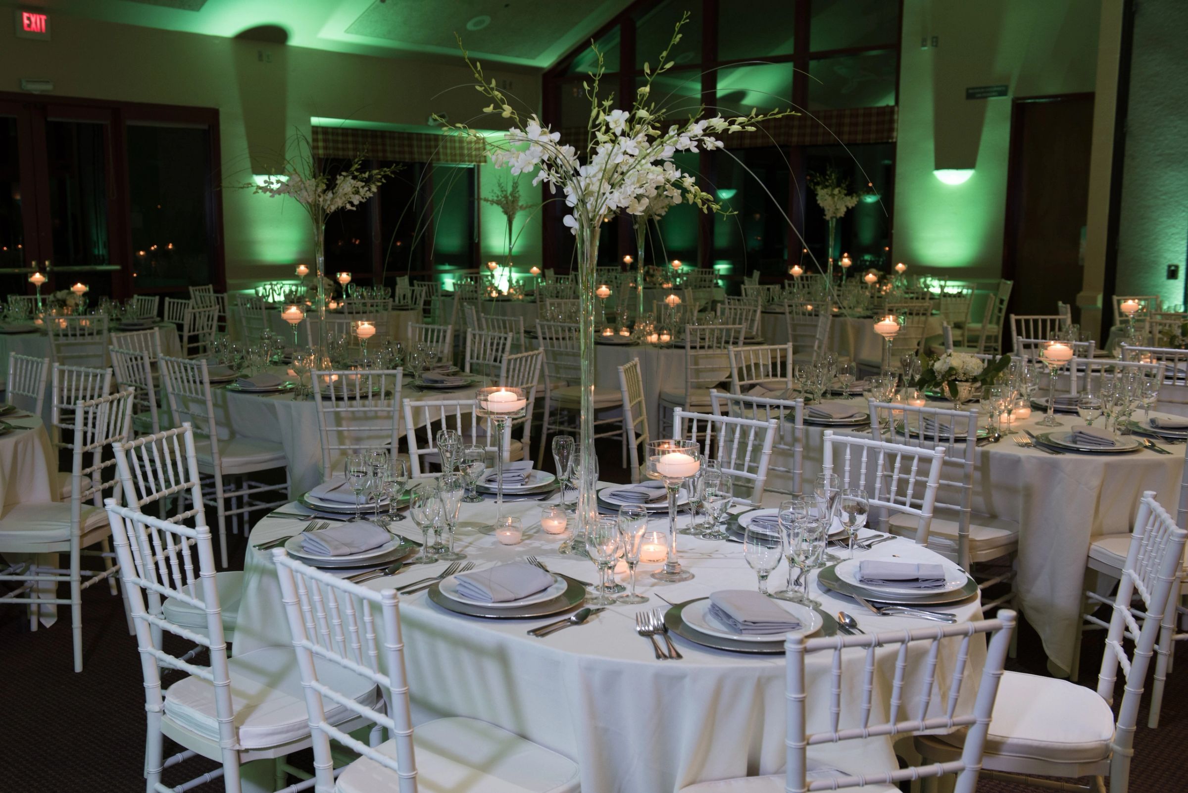 Reception room washed in green uplighting with tall floral centerpieces
