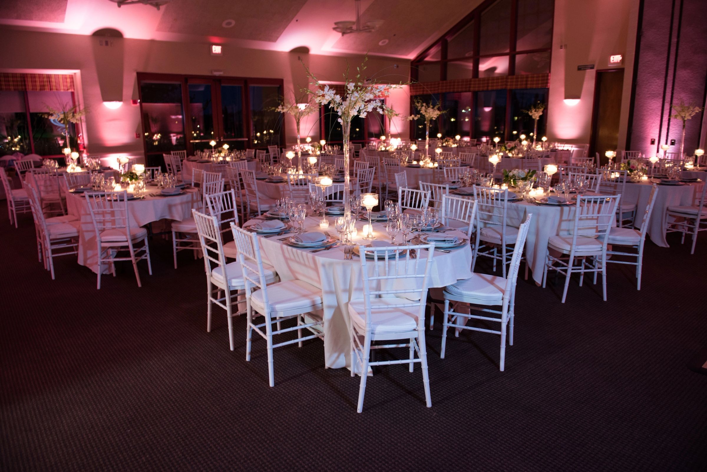 Reception room washed in pink uplighting with tall floral centerpieces
