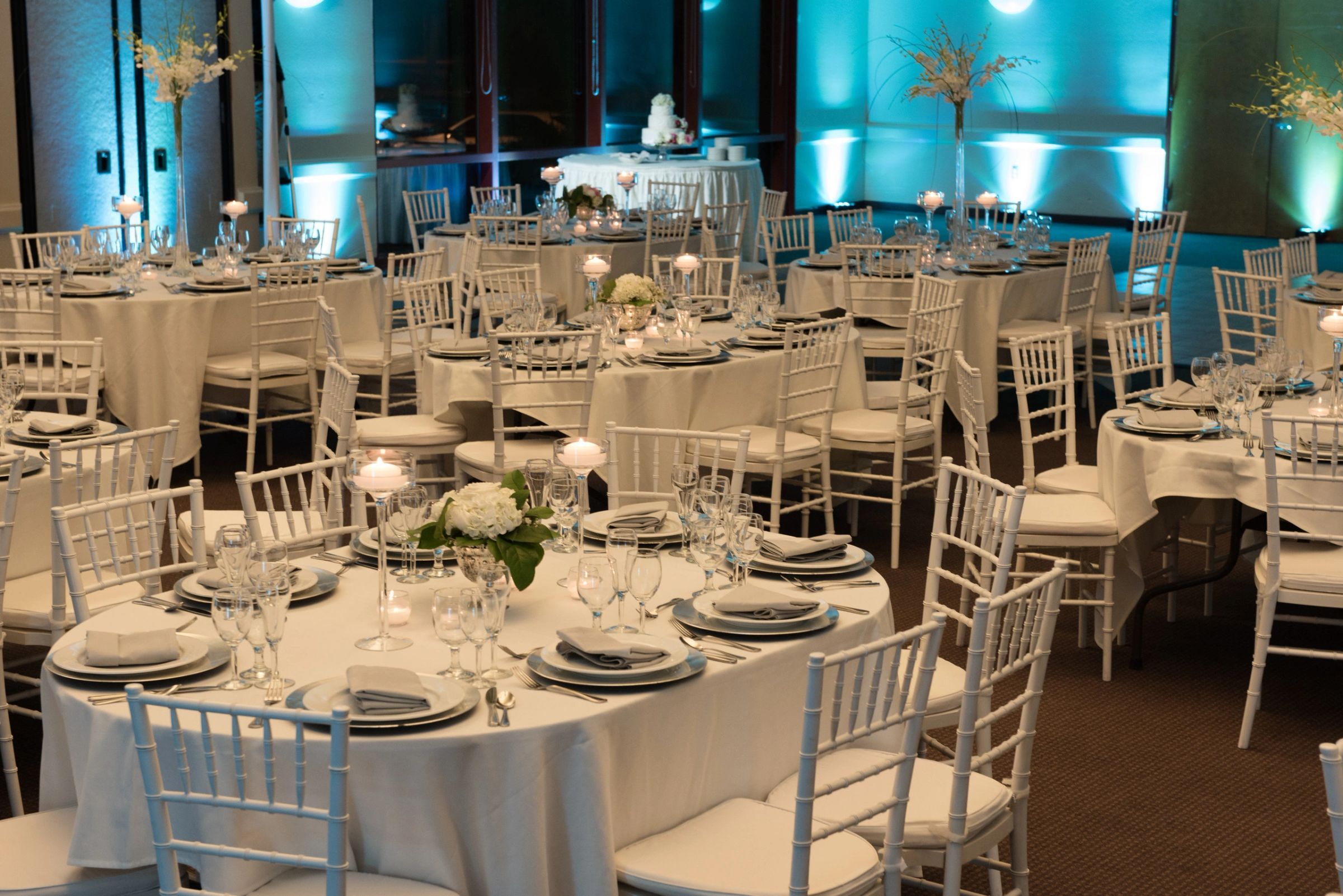 A reception room washed in teal uplighting with round tables set for dinner